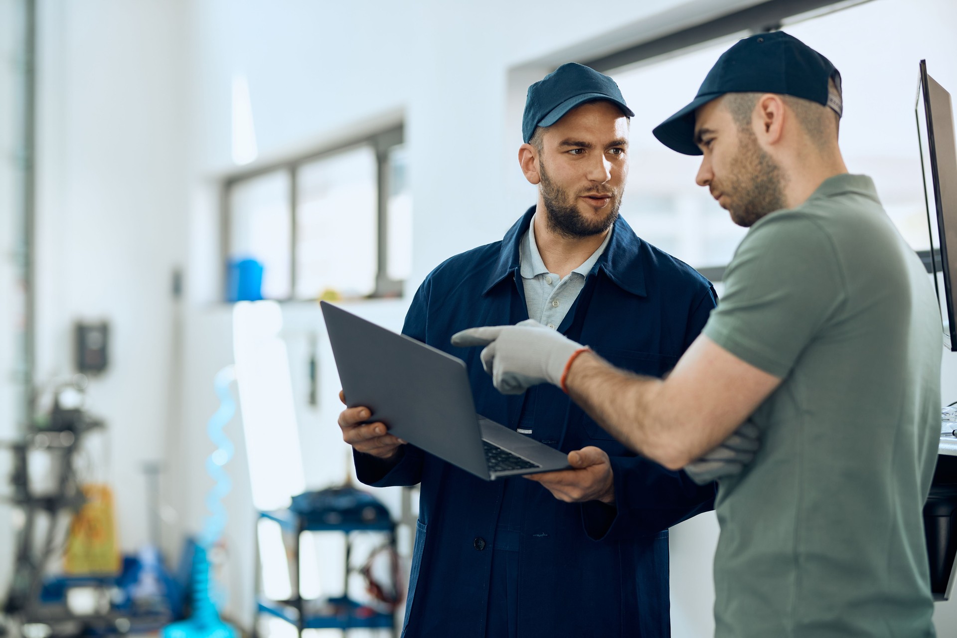 Two mechanics cooperating while working on laptop at auto repair shop.